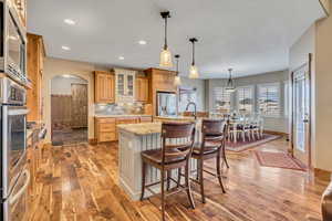 Kitchen with arched walkways, glass insert cabinets, an island with sink, a kitchen breakfast bar, and hanging light fixtures
