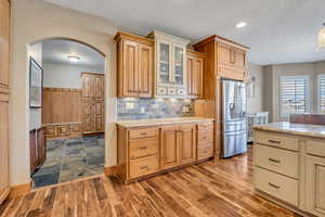 Kitchen featuring arched walkways, light stone counters, glass insert cabinets, stainless steel refrigerator with ice dispenser, and a textured ceiling