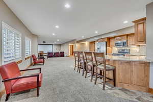 Bar area with light stone countertops, stainless steel appliances, decorative backsplash, light carpet, and recessed lighting