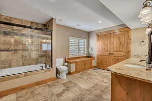Bathroom with bath / shower combo with glass door, double vanity, stone tile flooring, and recessed lighting