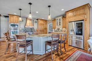 Kitchen with glass insert cabinets, stainless steel appliances, a breakfast bar, light stone counters, and arched walkways