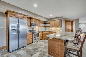 Kitchen with open shelves, stainless steel appliances, a peninsula, a breakfast bar, and light stone countertops