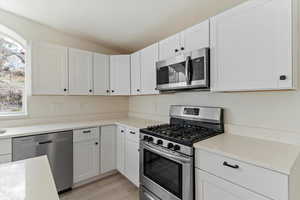 Kitchen featuring stainless steel appliances, white cabinets, light wood-style floors, vaulted ceiling, and light stone countertops