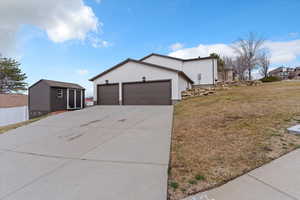 View of property exterior featuring concrete driveway, a garage, stucco siding, and a storage shed