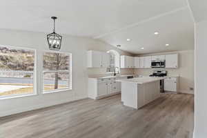 Kitchen featuring pendant lighting, white cabinetry, a center island, stainless steel appliances, and light wood-type flooring