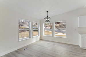 Unfurnished dining area featuring light wood-style floors, a chandelier, and lofted ceiling