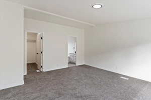 Unfurnished bedroom featuring a walk in closet, carpet floors, and ensuite bath