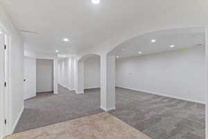 Below grade area with light carpet, arched walkways, and recessed lighting