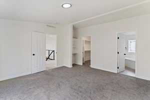 Unfurnished bedroom with a walk in closet, light colored carpet, and ensuite bathroom