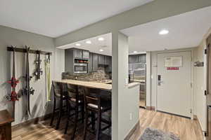 Kitchen with stainless steel fridge, light wood-style floors, recessed lighting, decorative backsplash, and a breakfast bar area