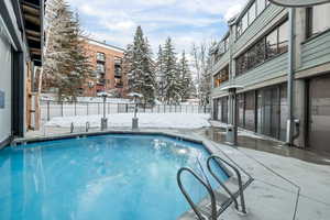 Snow covered pool with a patio area, a fenced backyard, and a community pool
