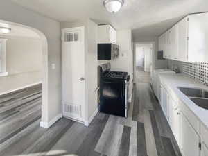 Kitchen featuring white cabinetry, appliances with stainless steel finishes, arched walkways, a textured ceiling, and light stone countertops