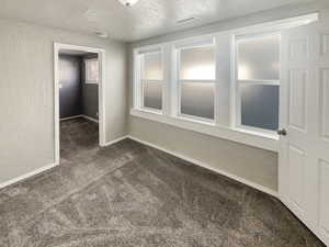 Empty room featuring a textured wall, a textured ceiling, and dark colored carpet