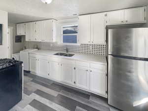 Kitchen with freestanding refrigerator, white cabinets, a textured ceiling, dark flooring, and washer / clothes dryer