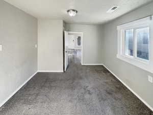 Unfurnished room featuring a textured wall, a textured ceiling, and dark colored carpet