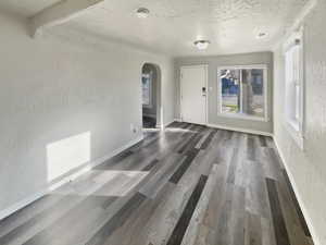 Unfurnished living room with a textured wall, arched walkways, a textured ceiling, and dark wood-type flooring