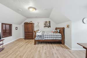 Bedroom with vaulted ceiling, light wood-style floors, and a textured ceiling