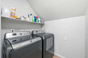 Laundry area featuring washing machine and dryer, vaulted ceiling, and a textured ceiling