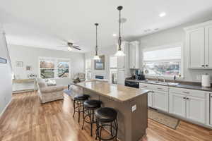 Kitchen with a kitchen island, white cabinets, a kitchen breakfast bar, light wood finished floors, and a ceiling fan