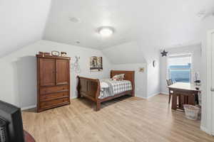 Bedroom with vaulted ceiling, light wood-type flooring, and a textured ceiling