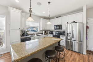 Kitchen featuring a breakfast bar, black appliances, dark wood-style flooring, decorative light fixtures, and recessed lighting