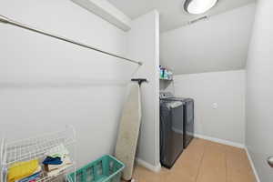 Laundry room featuring vaulted ceiling, independent washer and dryer, and light tile patterned floors