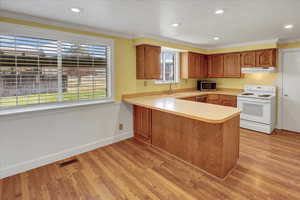 Kitchen featuring stainless steel appliances, brown cabinets, light countertops, a peninsula, and ornamental molding