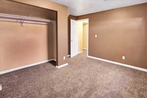 Unfurnished bedroom with a textured ceiling, carpet flooring, and a closet