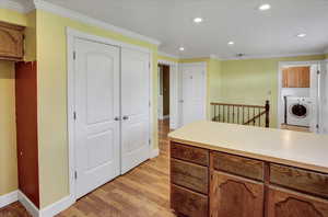Kitchen featuring crown molding, light countertops, brown cabinets, washer / clothes dryer, and light wood finished floors