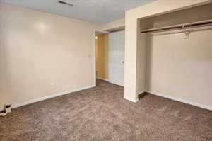 Unfurnished bedroom featuring a textured ceiling, carpet, and a closet