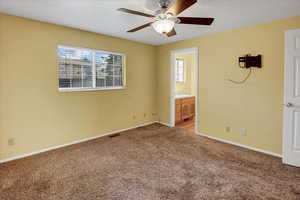 Unfurnished bedroom with multiple windows, carpet floors, ensuite bathroom, and a ceiling fan