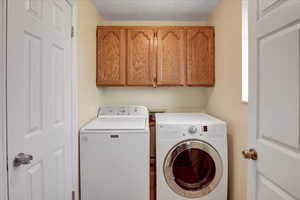 Laundry area with cabinet space, independent washer and dryer, and a textured ceiling