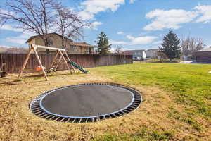 Fenced backyard featuring a trampoline, a playground, and a residential view