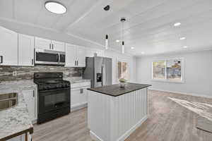 Kitchen featuring white cabinetry, appliances with stainless steel finishes, a center island, decorative light fixtures, and light wood-style floors