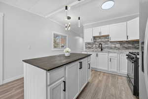 Kitchen featuring wood counters, white cabinets, black gas range oven, pendant lighting, and beamed ceiling