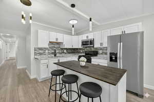 Kitchen with stainless steel appliances, a kitchen bar, butcher block counters, and white cabinets