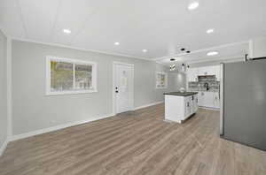Kitchen featuring dark countertops, freestanding refrigerator, ornamental molding, white cabinets, and a center island