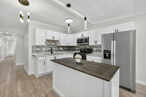 Kitchen with butcher block countertops, appliances with stainless steel finishes, white cabinetry, a kitchen island, and decorative backsplash