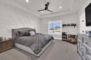 Bedroom with light colored carpet, recessed lighting, a ceiling fan, a tray ceiling, and a decorative wall