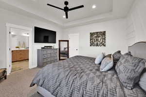 Bedroom featuring light carpet, a tray ceiling, recessed lighting, a ceiling fan, and ensuite bath