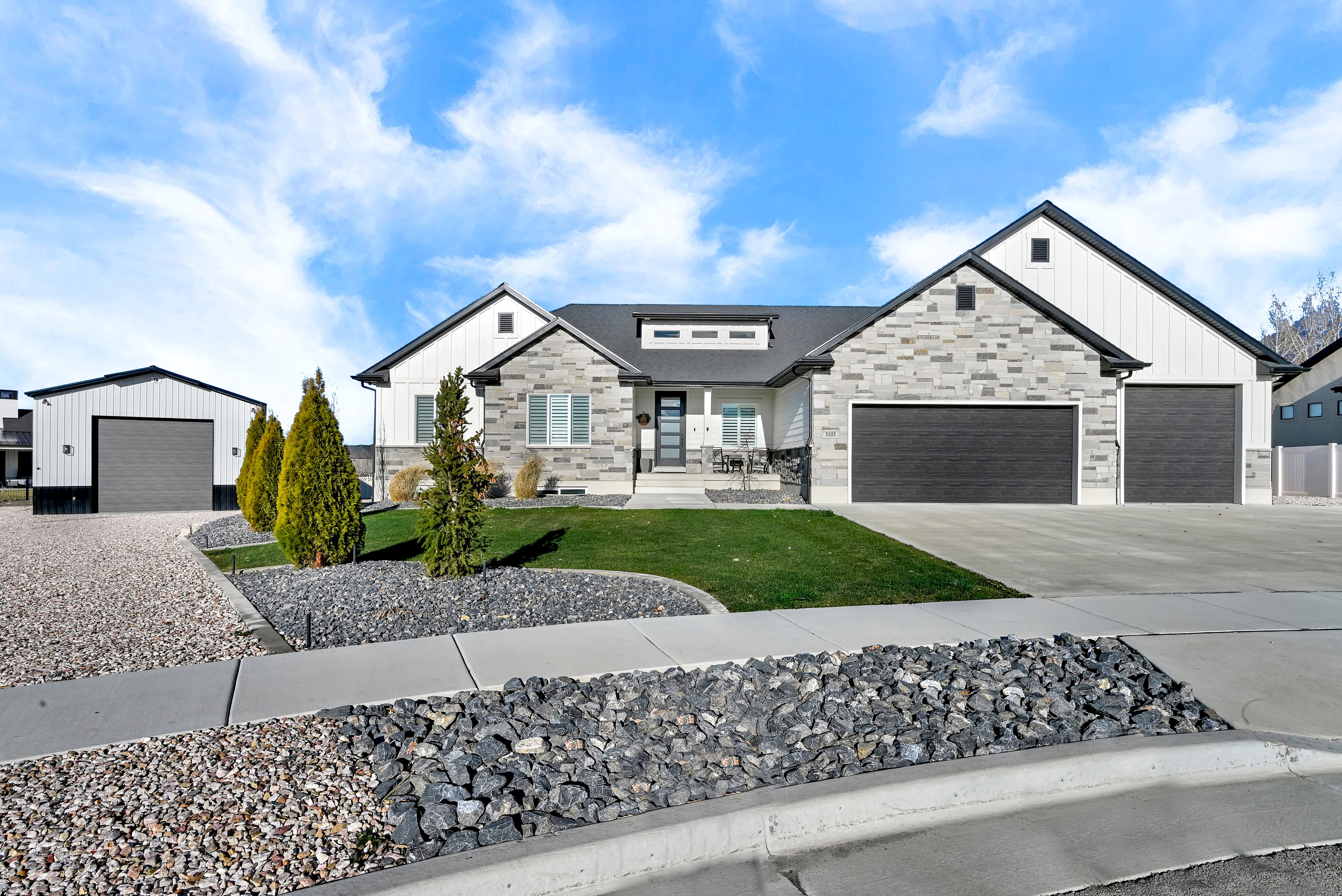 Modern farmhouse with board and batten siding, stone siding, a front yard, and driveway