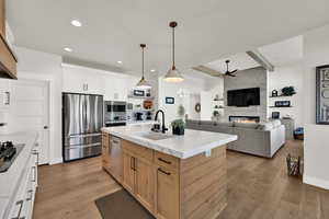Kitchen featuring hanging light fixtures, appliances with stainless steel finishes, light brown cabinetry, open floor plan, and light wood-style flooring