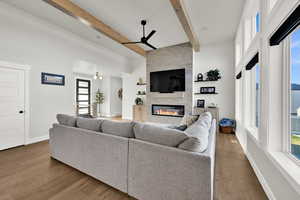 Living room with ceiling fan, a large fireplace, beam ceiling, and light wood finished floors