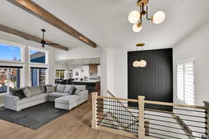 Living room with a chandelier, light wood finished floors, beamed ceiling, and a ceiling fan
