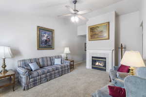 Carpeted living area with vaulted ceiling, a tile fireplace, and a ceiling fan