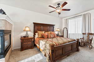 Bedroom with light colored carpet, ceiling fan, a tile fireplace, and a textured ceiling