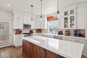 Kitchen featuring white cabinets, appliances with stainless steel finishes, decorative light fixtures, glass insert cabinets, and recessed lighting