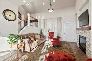 Living room with a stone fireplace, stairs, dark wood-style flooring, and recessed lighting