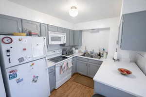 Kitchen with gray cabinetry, white appliances, light countertops, a textured ceiling, and light wood-style floors
