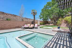 View of pool featuring a patio area, a fenced backyard, a pool with connected hot tub, and an area to practice putting